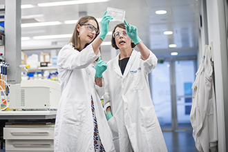 Two female researchers in laboratory, looking at research sample