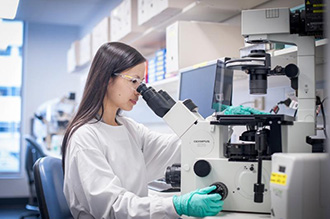 Dr Charis Teh in lab looking down microscope