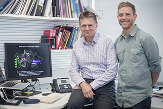 Two scientists standing in an office with a diagram of a structure on a computer screen next to them