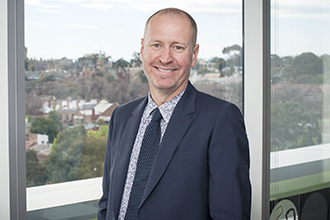 Doug Hilton stands smiling in office