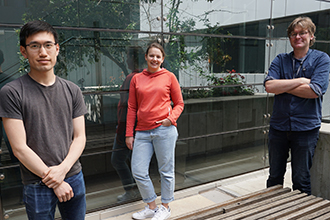 Three researchers standing in front of windows, looking at camera