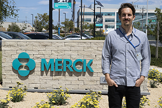 Smiling researcher in front of sign saying "Merck"