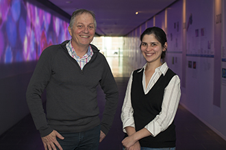 Two scientists standing smiling at camera in a long hallway with animation in the background