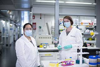 Two scientists in a laboratory wearing facemasks, lab coats and safety glasses