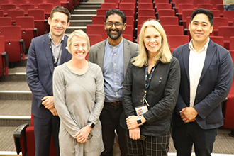 Photograph of five scientists in an auditorium