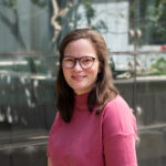 Rhea Longley is photographed sitting outside, wearing a brightly coloured top