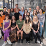 17 members of the Breast Cancer Lab are pictured together for a group photo on the WEHI balcony, all are facing the camera and smiling.