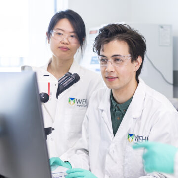 A student and supervisor working at a microscope