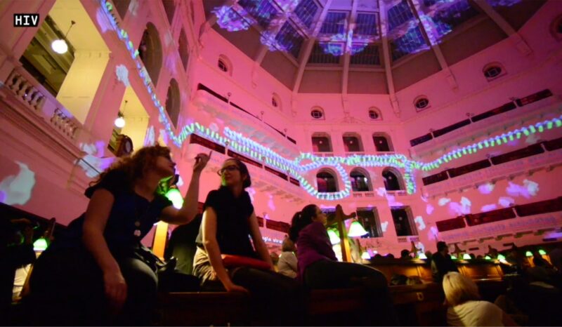 People sitting inside the State Library of Victoria with its interior illuminated in pink light.