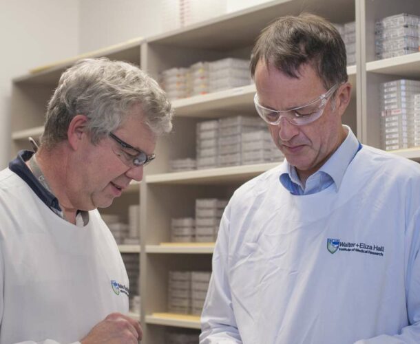 Two men. wearing white lab coats and safety glasses