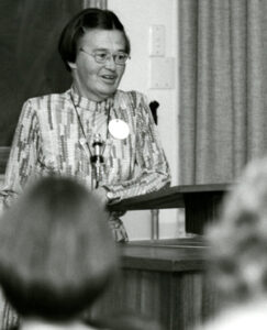 A woman with glasses giving a speech at a lecturn