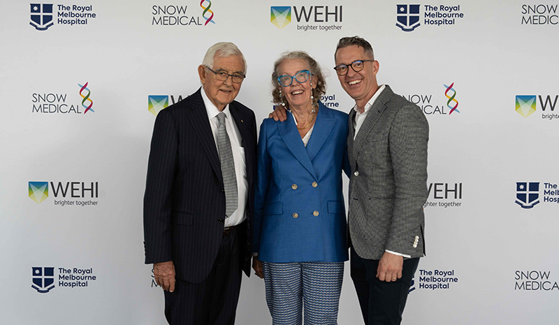 Terry Snow AM, Ginette Snow and Tom Snow photographed side-by-side. Behind them is a banner with logos of Snow Medical, WEHI and The Royal Melbourne Hospital