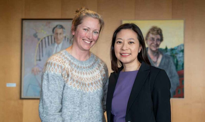 Assoc Prof Tracy Putoczki and Dr Belinda Lee are photographed standing side-by-side inside a room with paintings visible behind them.