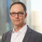 Head-and-shoulders photo of Dr Chris Burns with a city view in the background