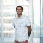 Vihanda Wickramasinghe photographed in a light-filled corridor, smiling at the camera
