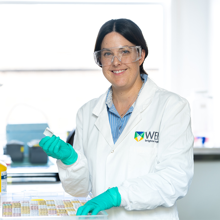 Dr Clare Weeden is photographed in a laboratory, smiling at the camera and holding scientific equipment