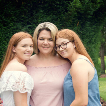 A photo of three women smiling at the camera, photographed outdoors