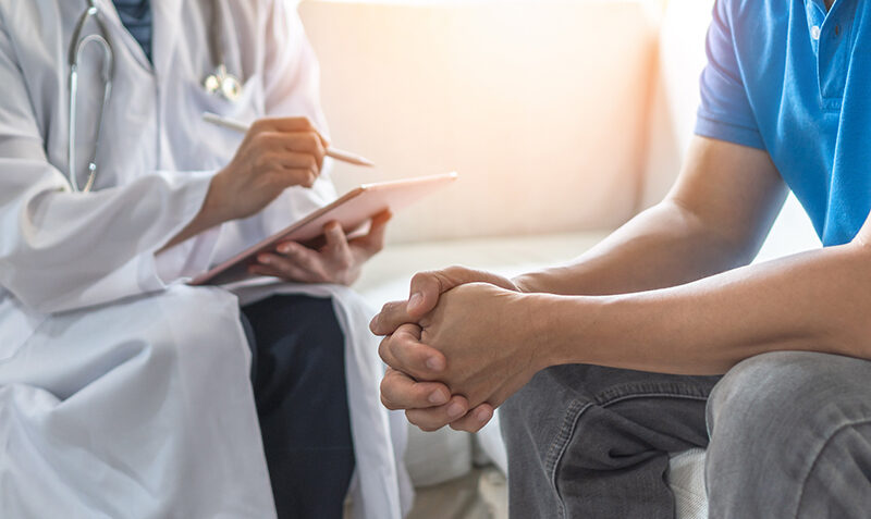 A patient's hands are visible, with a doctor in the background